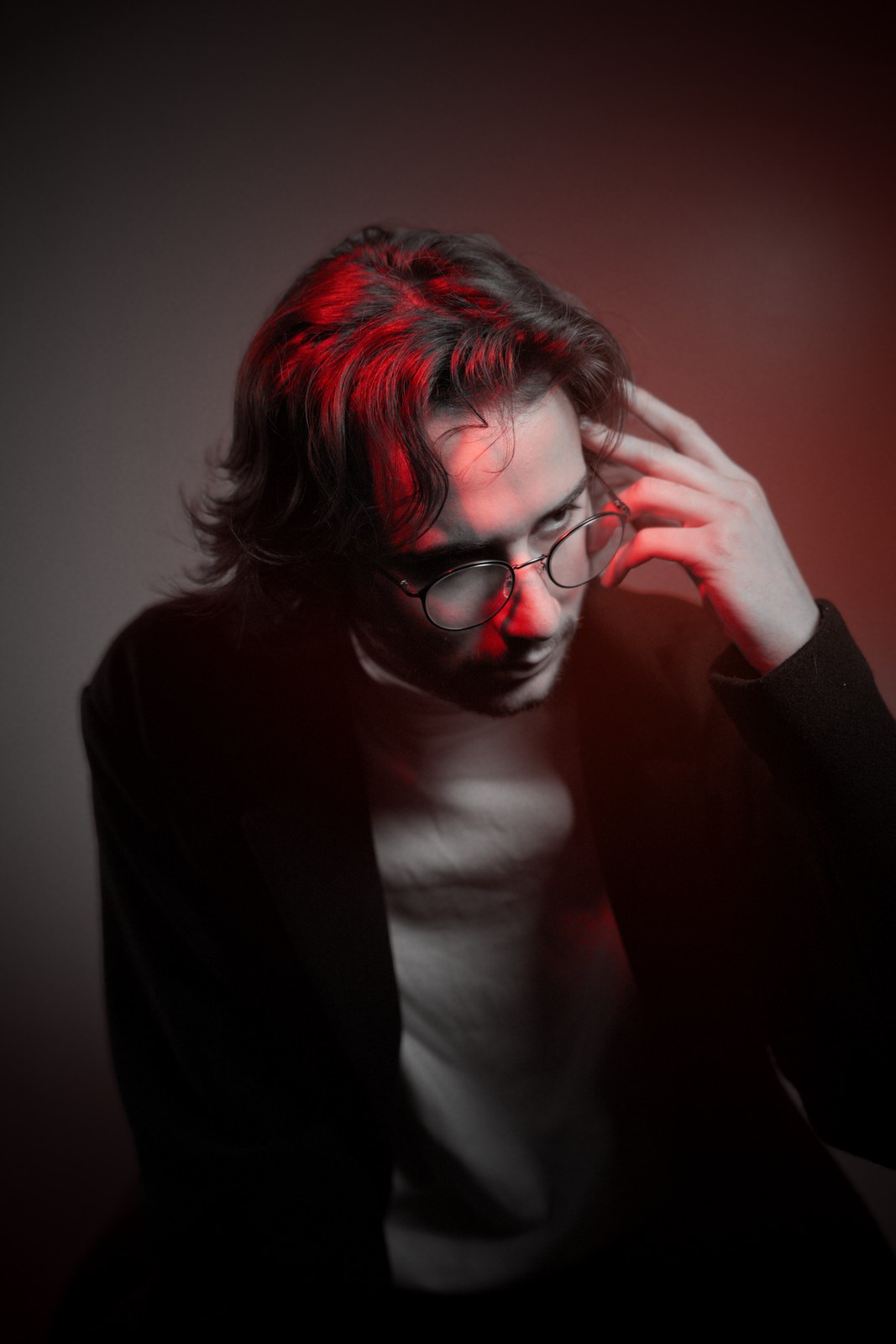 Portrait with red light, head lowered and one hand raised to the hair.