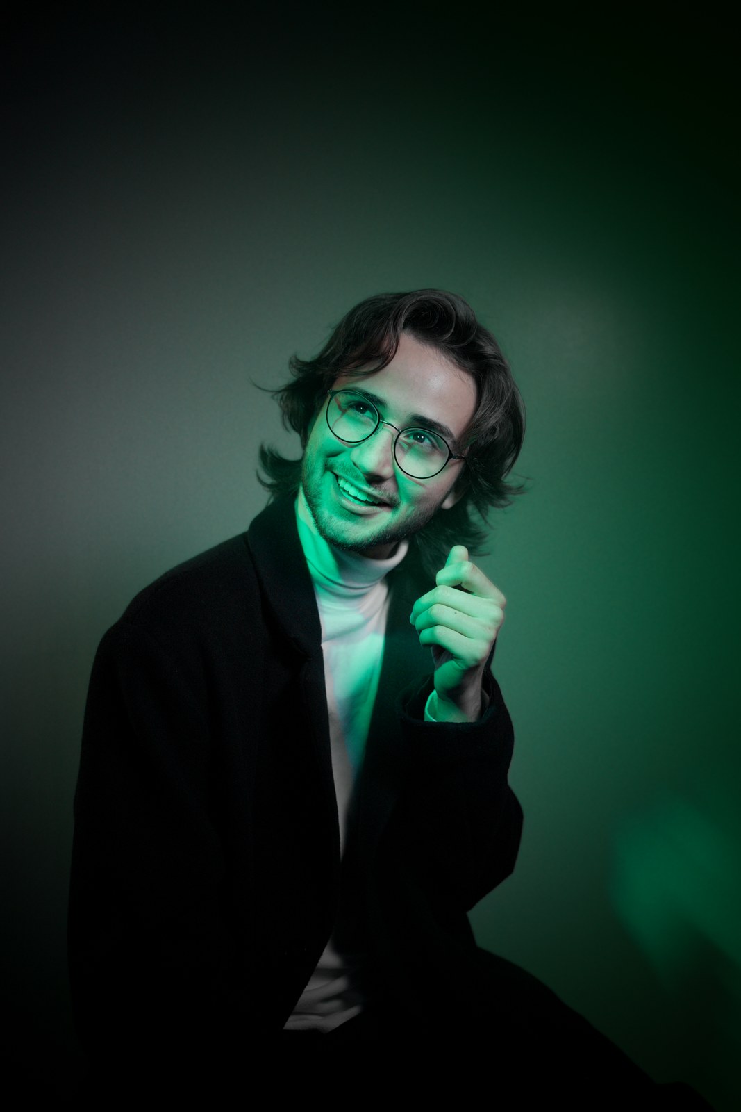Portrait in green light with one hand held beside the face.