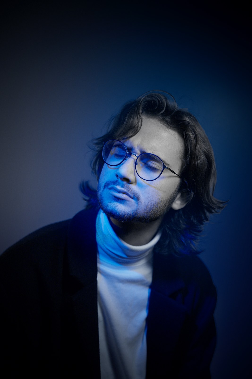 Portrait in blue light, looking upward through glasses.