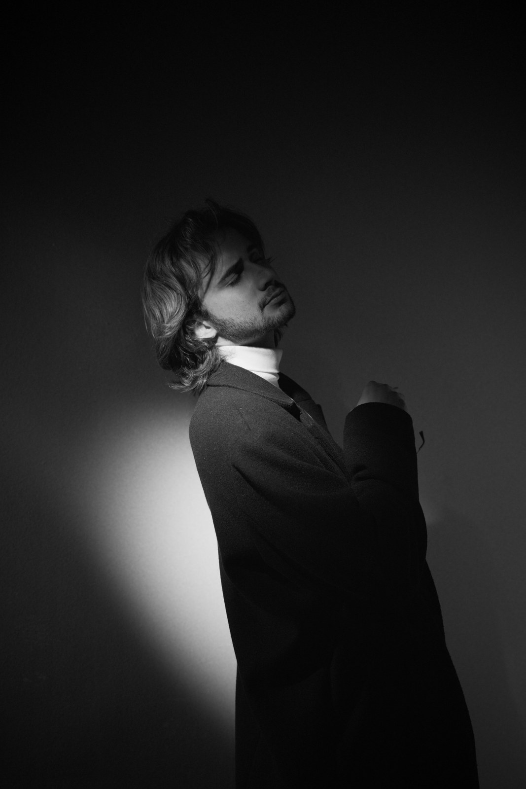 Black-and-white portrait turning over one shoulder toward the light.