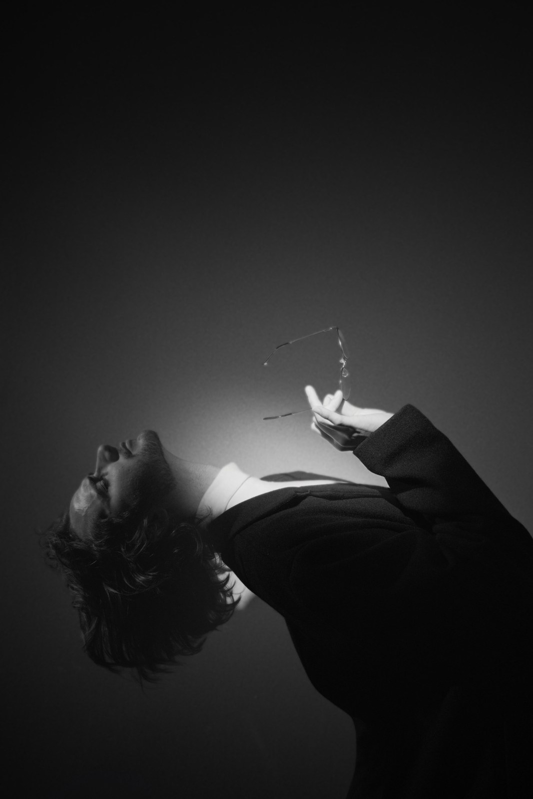 Black-and-white portrait leaning back with one hand raised into the light.