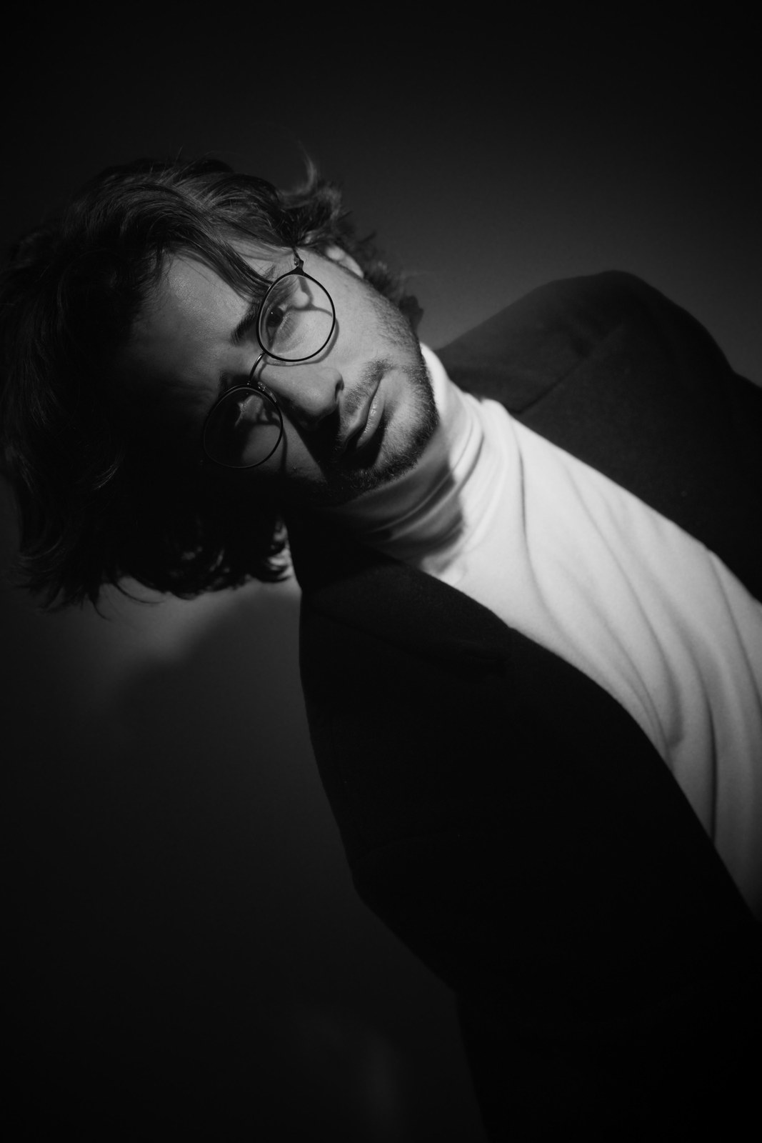 Black-and-white portrait with head tilted sideways and a hand in the hair.