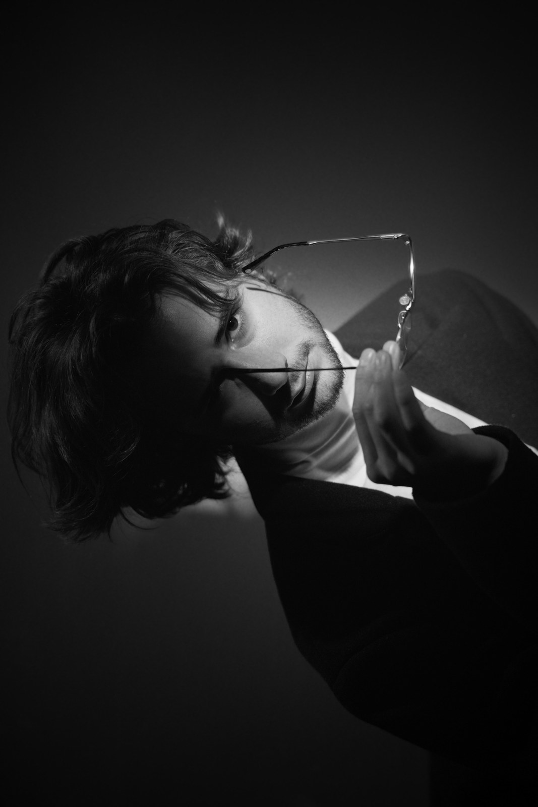 Black-and-white portrait holding glasses near the mouth.