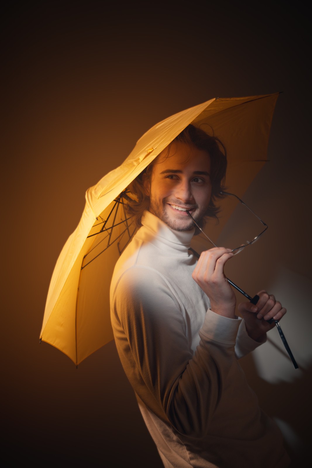 Smiling portrait beneath a yellow umbrella in warm light.
