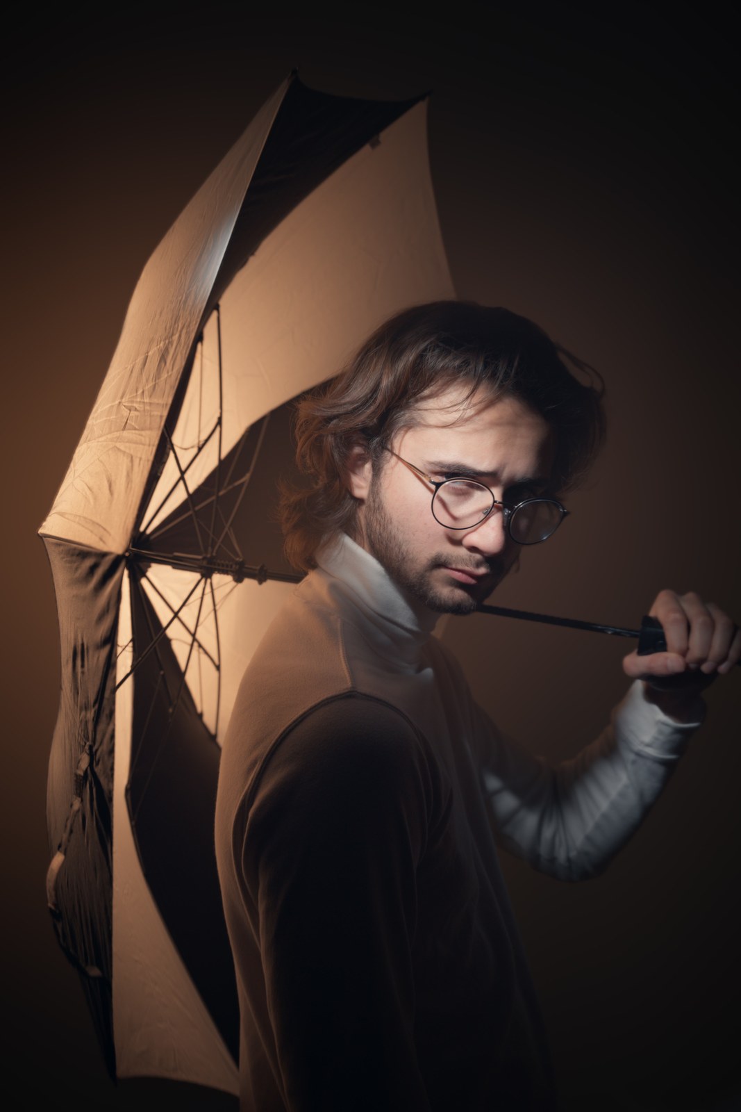 Portrait looking over one shoulder with an umbrella and a raised hand.