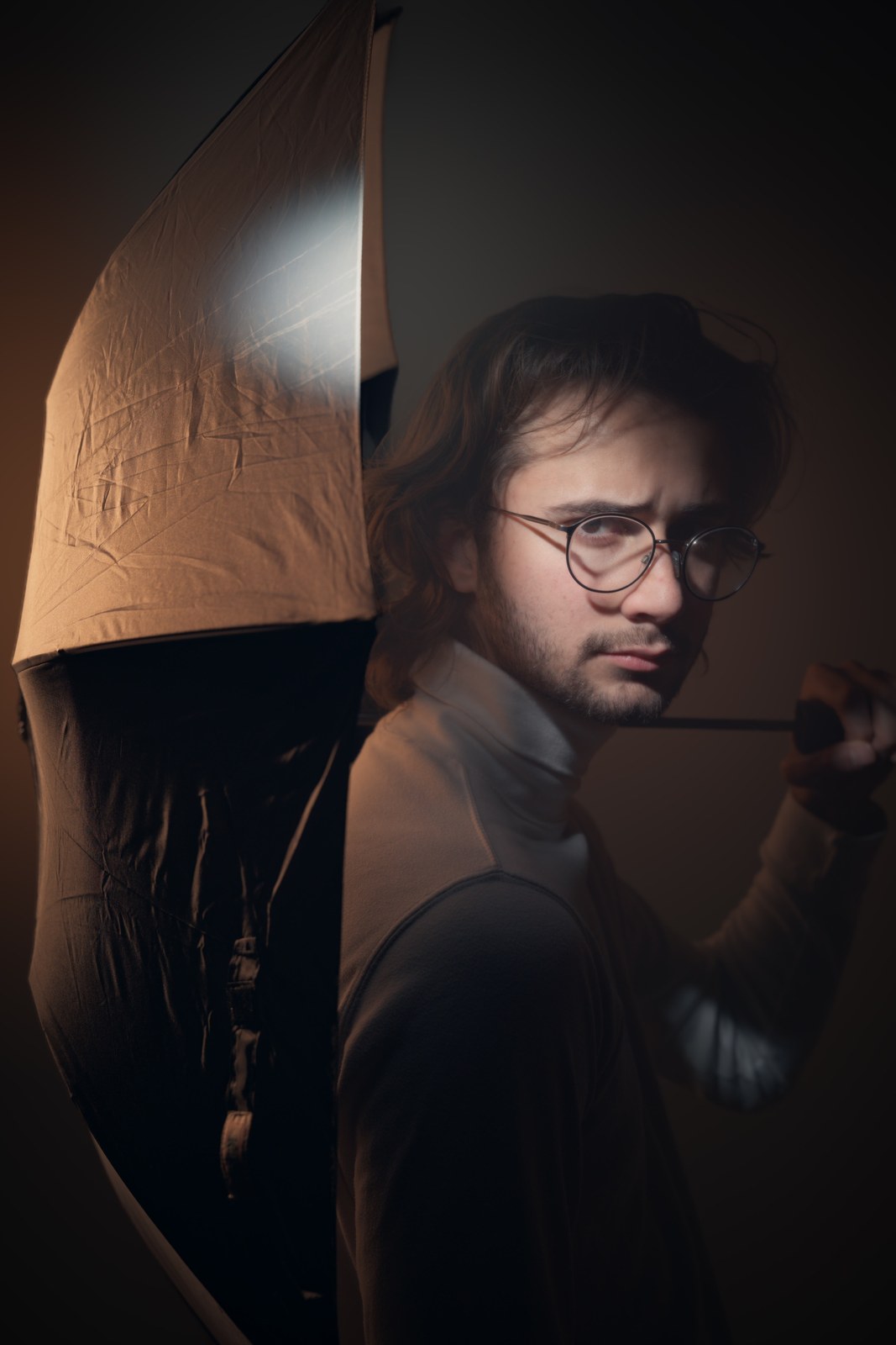Portrait looking toward the camera beneath an umbrella in warm side light.