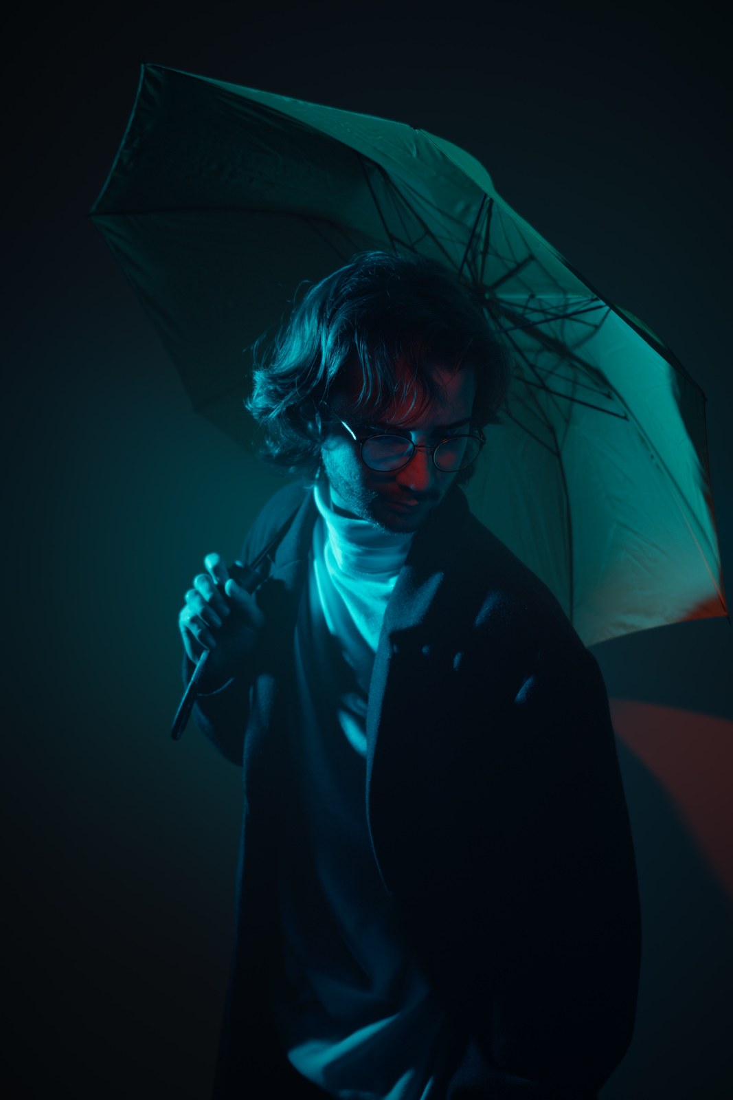 Portrait beneath a teal umbrella with a hand held near the face.