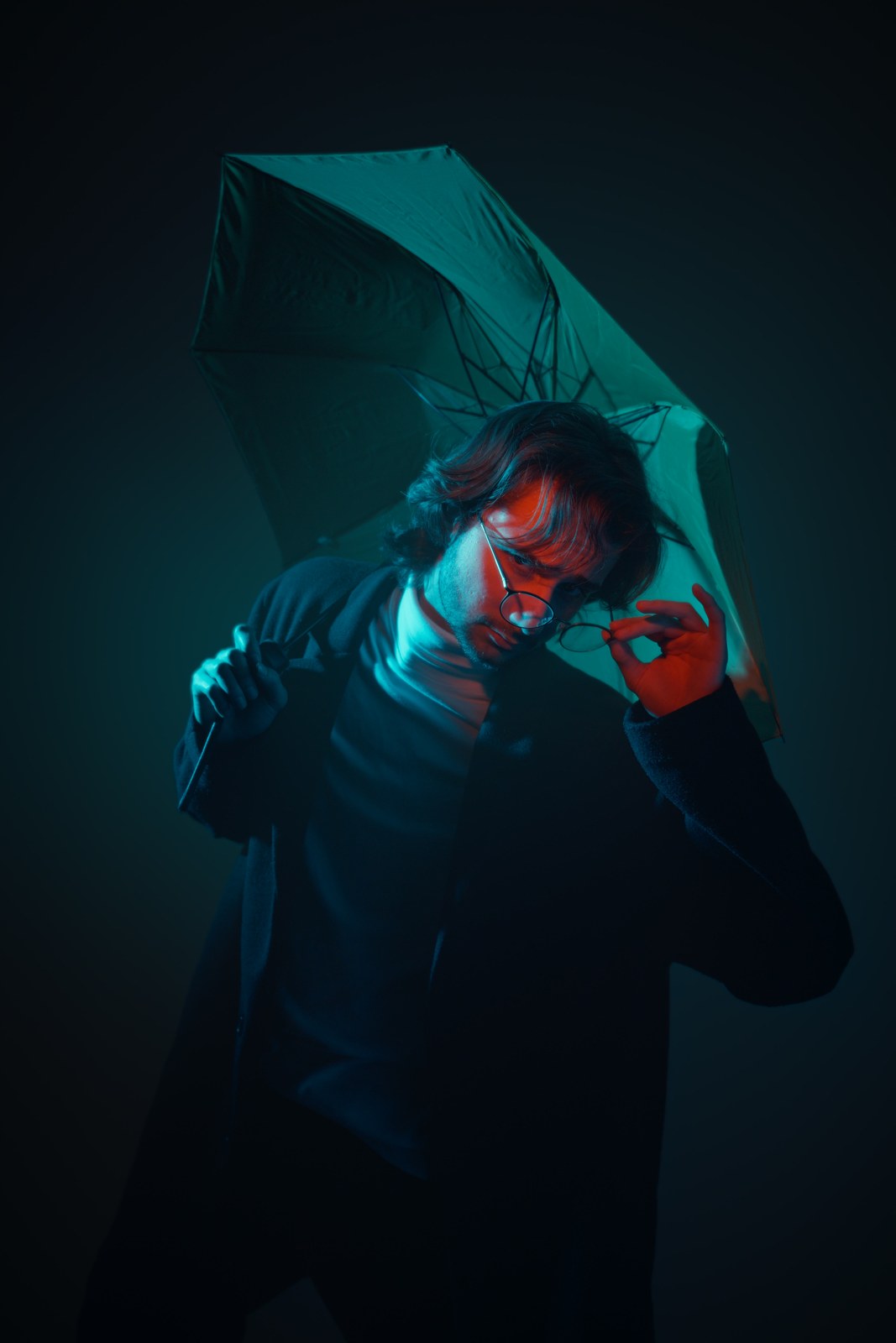 Portrait touching glasses beneath an umbrella in teal and red light.
