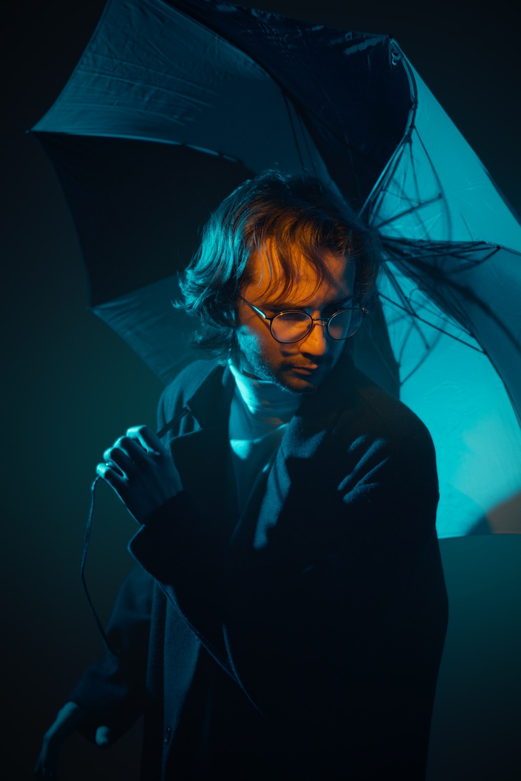 Portrait leaning forward beneath a teal umbrella in warm side light.