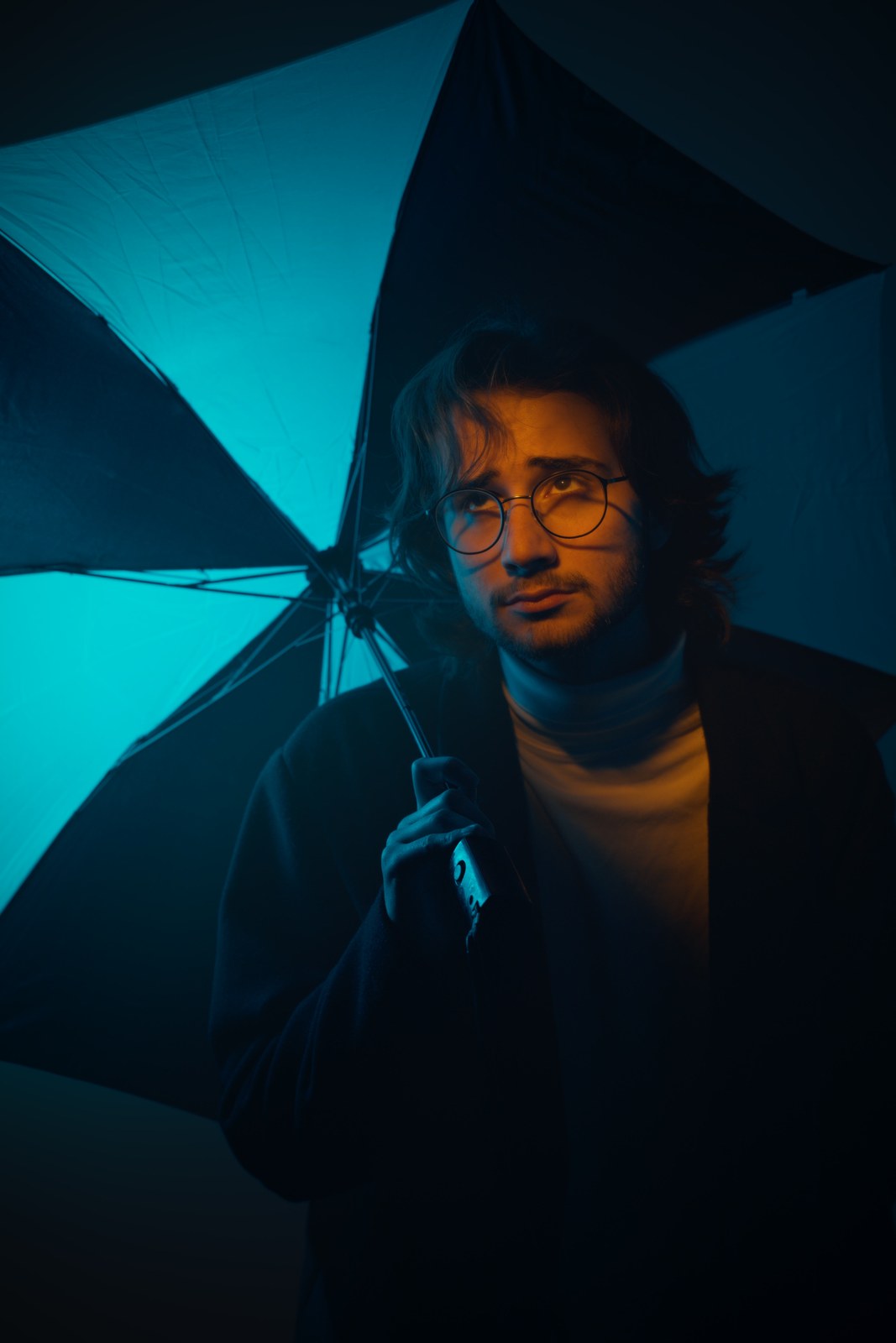 Portrait holding an umbrella beside the face in blue-green light.