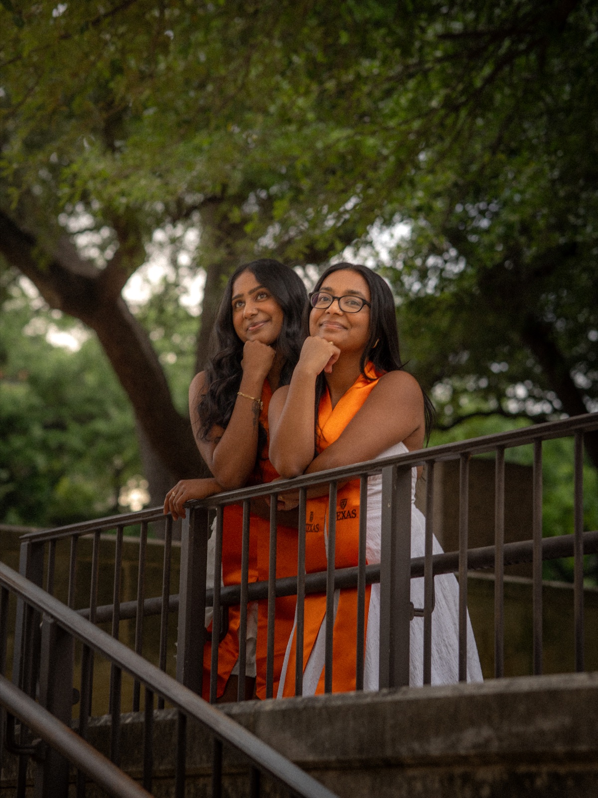 Two graduates in orange stoles posing together on an outdoor staircase.