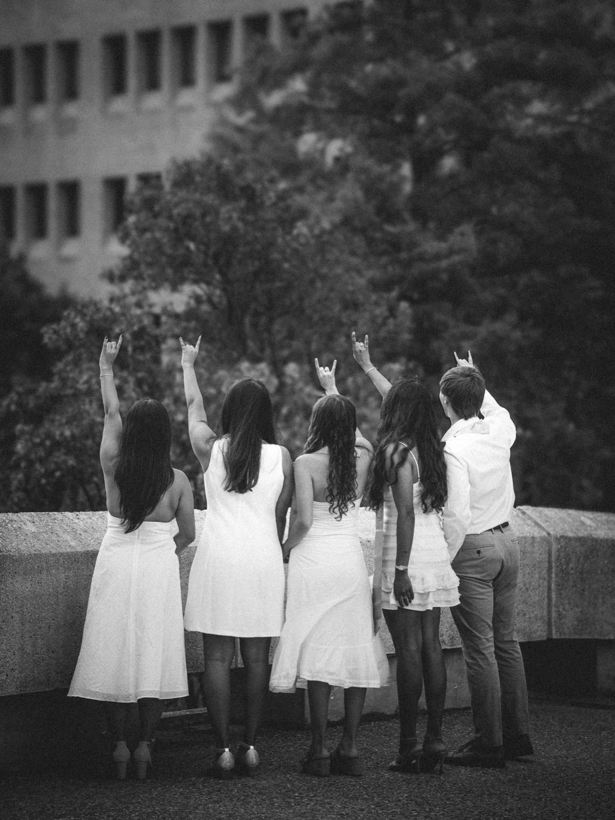 Black-and-white portrait of five friends facing away and raising their hands.